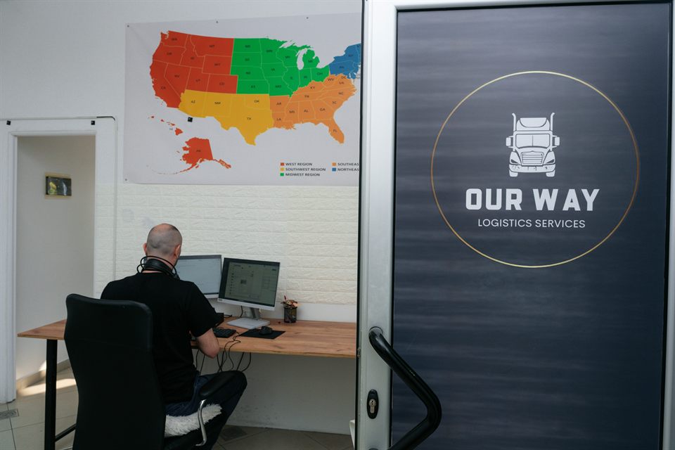 OUR WAY LOGISTICS branding on the office entrance beside a workstation